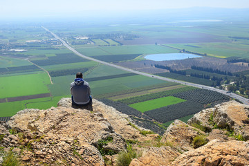 lonely man sits on the edge of a cliff and looks at the magnificent landscape of the Jezreel...