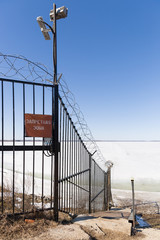 Metal fence with barbed wire and sign in Russian - Forbidden Zone -. Guarded territory with video surveillance. Winter concept. The reservoir is covered with ice.
