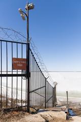 Fototapeta premium Metal fence with barbed wire and sign in Russian - Forbidden Zone -. Guarded territory with video surveillance. Winter concept. The reservoir is covered with ice.