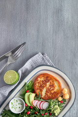 Fried round slice of cheese with green rucola salad with avocado, radish and pomegranate seeds, copy-space