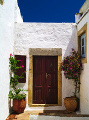 Fototapeta na wymiar Beautiful white house with brown wooden door, ceramic pots with flowers and deep blue summer sky. Patmos island, Greece
