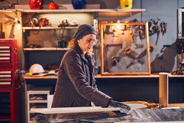 Woman carpenter sanding old window in a retro workshop.