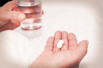 sick man in bed holding a glass of water and pill