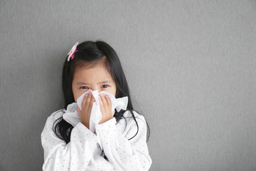 Asian child or kid girl sick and sad with sneezing on nose and cold cough on tissue paper because...