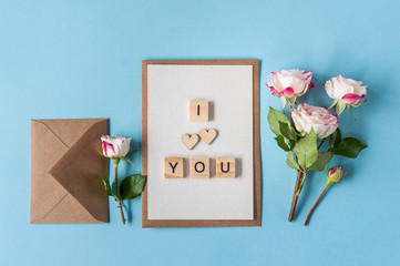 Coral roses with wooden letters spelling I love you  on blue background. Minimalism, soft focus, top view, flat lay, copy space.