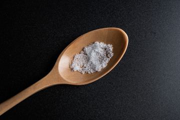 One scoop of fine lake salt on black background