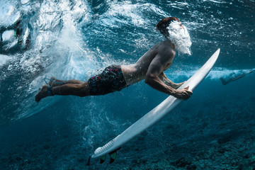 Surfer performs dive (the duck dive) with his surfboard under the wave and exhales air into the...