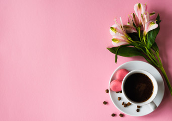 Cup of coffee with macaroons with coffee beans on a saucer with a pink flower on a pink background