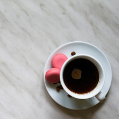 Cup of coffee with macaroons with coffee beans on a saucer on marble background