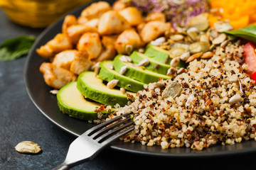 Salad with quinoa, avocado and chicken. Front view. Served on a black plate.