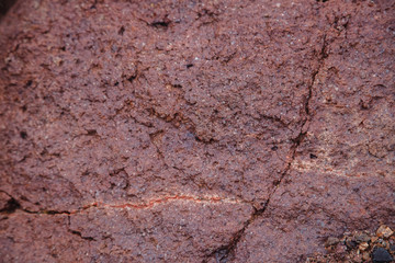 The texture is red and Burgundy. Rock wall with vegetation and crack