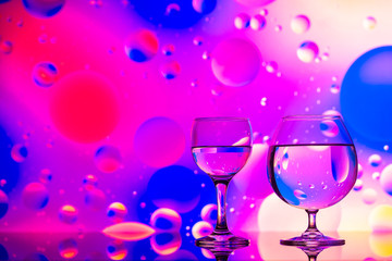 transparent glasses with water and oily drops on colorful background 