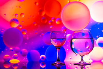 transparent glasses with water and oily drops on colorful background 