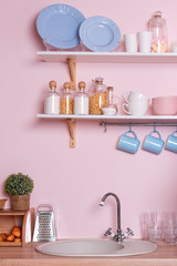 Pink and blue pastel modern kitchen interior. Kitchen accessories, containers with cereals, dishes and hanging blue cups.