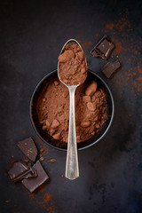 Cocoa powder in a spoon with chocolate chunks at the dark background. Overhead view
