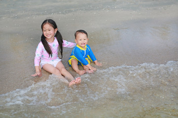 Obraz premium Smiling little Asian sister and her little brother in swimming suit playing sea waves on the beach.