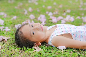 Naklejka na ściany i meble Smiling little girl lying on green grass with fall pink flower in the garden outdoor.
