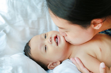 Asian Mother is playing and kissing her little baby boy on the bed. 