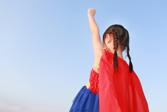 Little child girl Superhero in a gesture to fly on clear blue sky background. Kid super hero concept.
