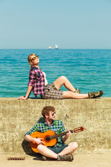 Young man playing guitar to his girlfriend by seaside