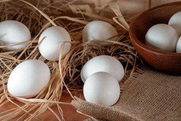 Chicken eggs lie in the straw on a wooden surface and a bowl. Easter