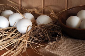 Chicken eggs lie in the straw on a wooden surface and a bowl. Easter