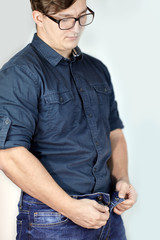 Young handsome caucasian man unzipps blue jeans. Man torso, fingerring, blue shirt, glasses....