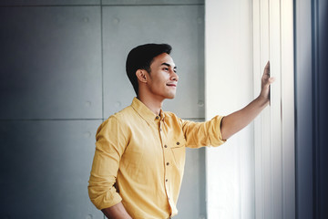 Portrait of Happy Businessman Standing by the Window in Office. Looking Away and Smiling. Dreaming...