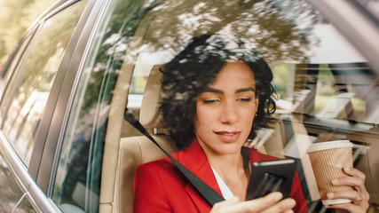 Beautiful Woman Traveling in a Car, Sitting on a Passenger Seat Uses Smartphone, types Message, Browses Through Internet, Holds Coffee. Camera Shot from Outside the Vehicle.