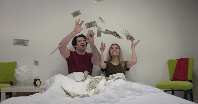 Couple in pajamas sitting in white bed and throwing money