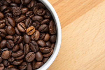 Coffee beans in a white cup on a wooden background.