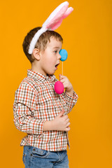 Portrait of cute little child boy with Easter bunny ears holding colorful eggs on yellow background. Happy easter