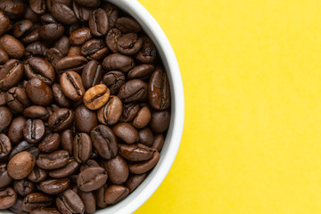 Coffee beans in a white cup on a yellow background, top view.