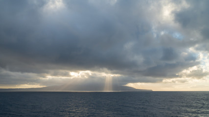 Sun rays burst out from behind clouds over the ocean