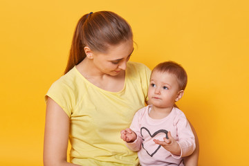 A joyful mother lookes after her adorable daughter . A woman gives a sweet gaze, checks how a cute baby counting. A smart kid sits at her mother`s knees and looks in her eyes attentively.