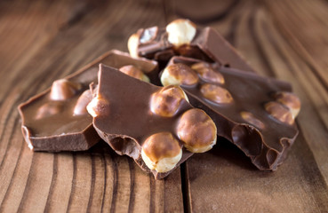 Heap of pieces of chocolate with whole nuts on wooden table.