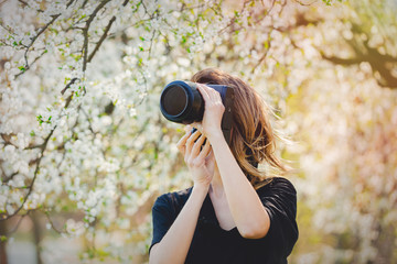 Young girl with camera stay near a flowering tree