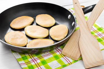 Pan with pancakes on the white woobed table. Cooking food.