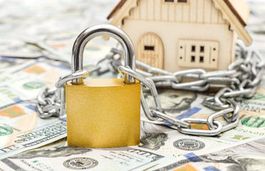 Model of house locked by chain with padlock on background of dollar bill.