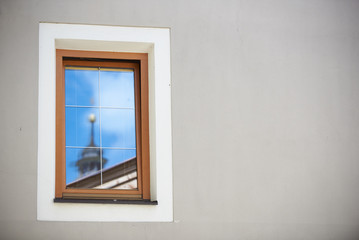 Ein Kirchturm in Tirol spiegelt sich im Fenster einer Hauswand