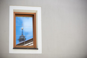 Fototapeta premium Ein Kirchturm in Tirol spiegelt sich im Fenster einer Hauswand
