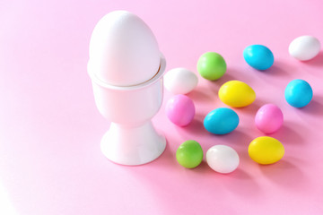White big egg in the stand and small colorful candy eggs. Easter celebrate concept. Pink background.