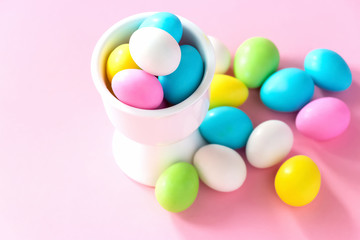Small colorful candy eggs in the stand. Easter celebrate concept. Pink background.
