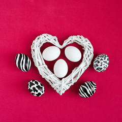 Easter eggs painted like zebra, cow, snow leopard. Three white eggs inside a white heart on red background. Top view.