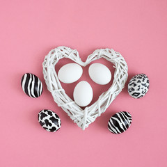 Easter eggs painted like zebra, cow, snow leopard. Three white eggs inside a white heart on pink background. Top view.