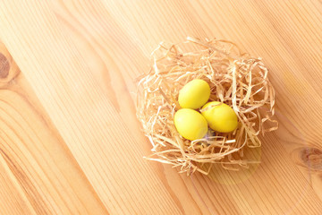 Three yellow eggs in a nest on a light wooden background. Easter celebrate concept.