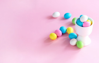 Small colorful candy eggs in the stand. Easter celebrate concept. Pink background.