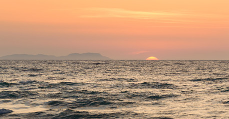 Corfu Sunset over the sea, in the background an island with an orange sun over the water.