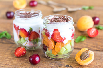 Homemade yogurt parfait with apricot, cherry, strawberry and kiwi fruit in a mason jar on rustic background. healthy breakfast