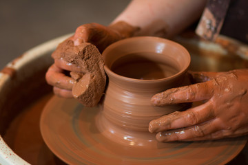 Rotating potter's wheel and clay ware on it taken from above. A sculpts his hands with a clay cup on a potter's wheel. Hands in clay. 